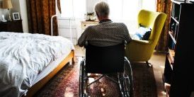 Senior in wheelchair sitting alone in small room facing a window
