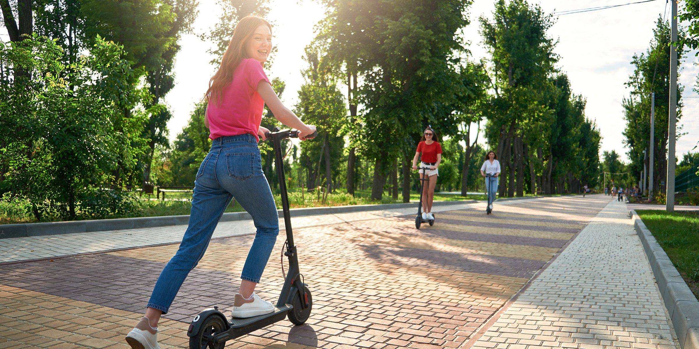 Three young friends riding e-scooters through a park
